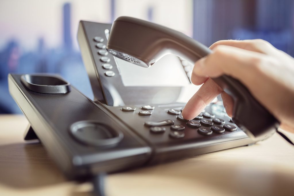 Hand lifting the handset of a desk telephone